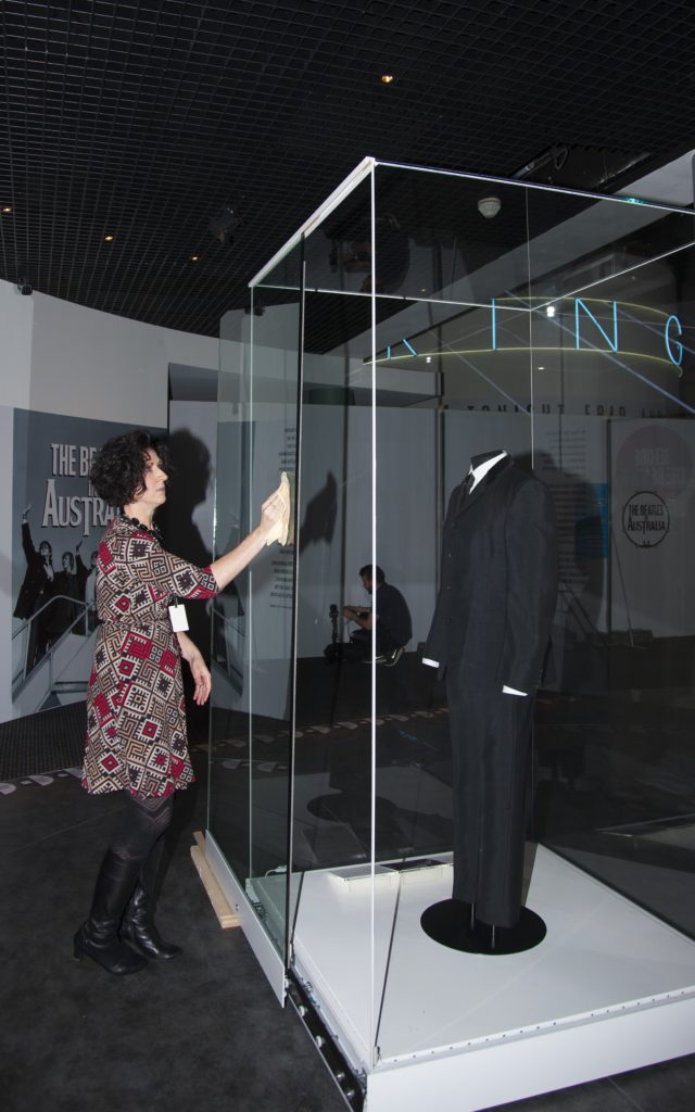 Registrar Katrina Hogan cleaning the showcase holding a suit worn by John Lennon